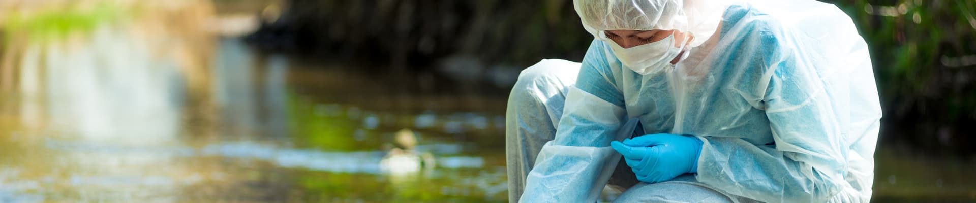 Un ricercatore in tuta protettiva preleva un campione d’acqua per l'analisi da un fiume inquinato